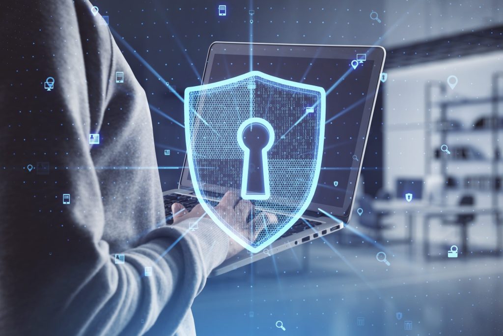 Hand using a laptop with a glowing cybersecurity shield hologram